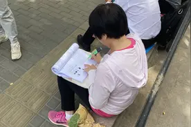 人大附中考点外 一位考生家长与学生同“做题”图片